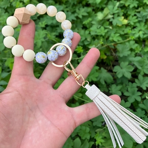 Handheld view of a beaded keychain featuring light blue foil beads and white leather tassel