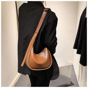 Sac bandoulière demi-lune en cuir marron avec sangle réglable porté par un mannequin
