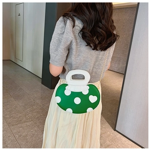 Detail view of a green and white apple-shaped crossbody bag with gold chain strap