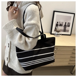 Detail of a large black and white striped canvas tote bag worn by a model in a cozy interior