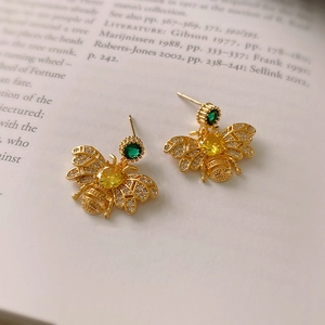 Macro detail of golden bee earrings with yellow stones and crystals on a book