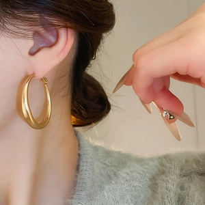 Close-up of model wearing large golden C-shaped hoop earrings with polished metal finish