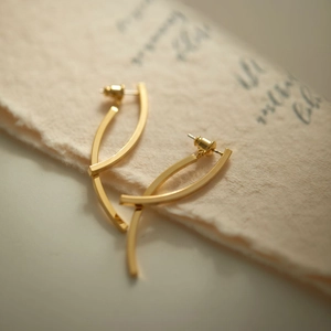 Close-up of gold geometric drop earrings with polished finish on a vintage paper background