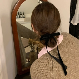 Elegant black velvet ribbon bow hair clip worn by a model in a cozy vintage setting