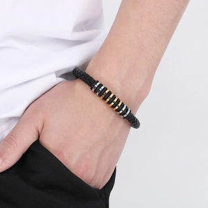 Close-up of men's braided black leather bracelet with gold and silver metal rings