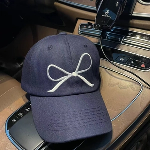 Navy blue cotton baseball cap with white bow embroidery shown on a car console