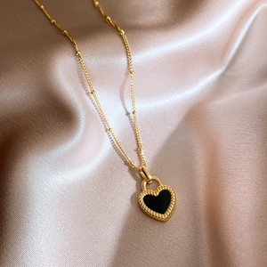 Double-sided black heart necklace in gold finish on champagne silk background