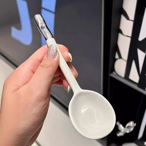Modern white ceramic soup spoon with silver-tone decorative handle tip on display