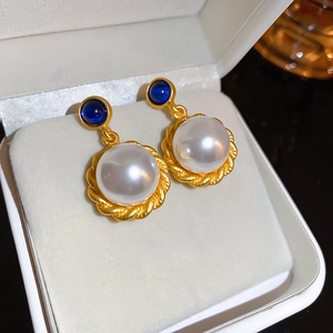 Macro view of vintage gold pearl earrings with blue gemstone detail in a gift box
