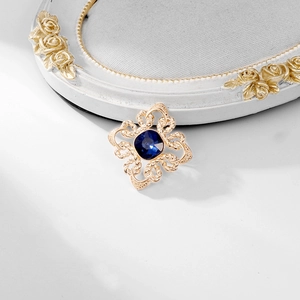 Close-up of a vintage gold brooch with a square blue crystal against a white background