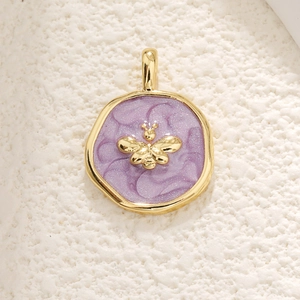 Macro detail of gold bee pendant with purple glitter enamel inlay and metal frame