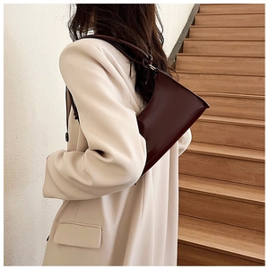 Deep burgundy glossy leather baguette bag worn over the shoulder by a model