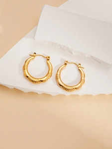 Detail of gold twisted ribbon hoop earrings with vintage metal texture on white stone
