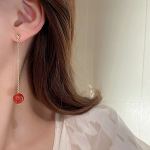 Detailansicht eines langen goldenen Quastenohrrings mit roter Perle am Ohr