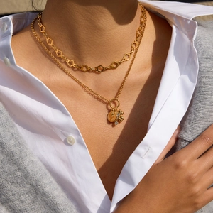 Close-up of layered 18K gold-plated clover and coin pendant necklaces on model