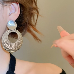 Gros plan d'une boucle d'oreille créole argentée avec texture perlée sur l'oreille