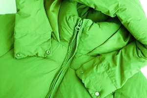 Detail der lindgrünen Daunenjacke mit Frontreißverschluss und Metallic-Druckknöpfen