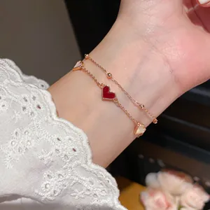 Close-up of rose gold double-layer bracelet with red heart and white shell pendant