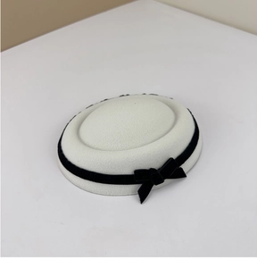 Detail of white wool felt pillbox hat with black velvet ribbon and delicate bow