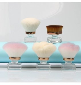 Detail of five makeup brushes with crystal handles and rose gold ferrules on blue background