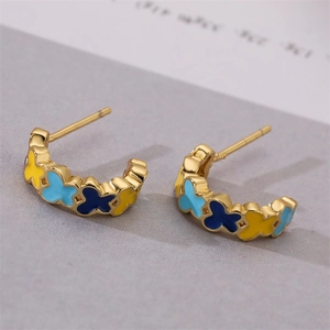 Macro shot of gold-plated C-shape earrings with colorful enamel butterfly motifs