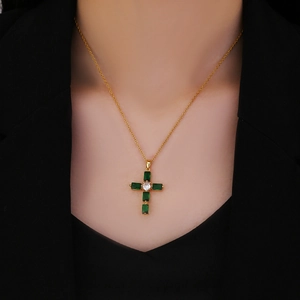 Primer plano de collar dorado con cruz de circonitas verde esmeralda sobre ropa negra