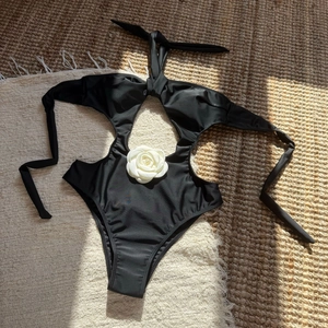Close-up of a white 3D camellia flower on a black cutout one-piece swimsuit