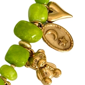 Green beaded bracelet with golden heart moon star and teddy bear charms on white background