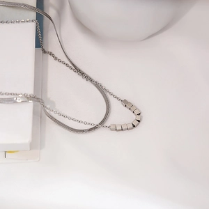 Macro detail of silver layered snake chain necklace with a brushed metal square pendant