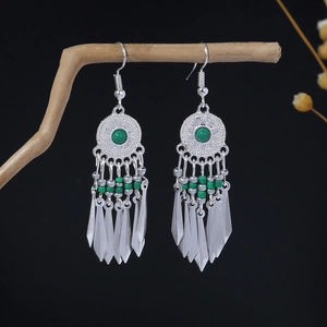 Bohemian silver drop earrings with green beads and metal tassels on a wooden branch