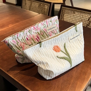 Canvas makeup bag with tulip embroidery and floral pattern on a wooden surface