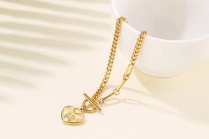 Detail of gold titanium steel heart pendant bracelet with T-bar clasp on a white bowl