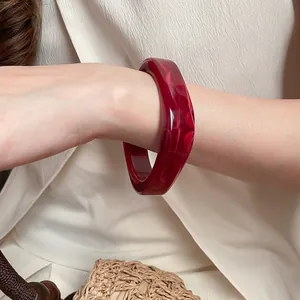 Elegant wide red acrylic resin bangle with irregular geometric cut worn by model