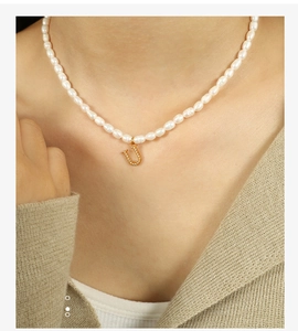 Close-up of pearl necklace with a gold letter U pendant featuring micro-inlaid details