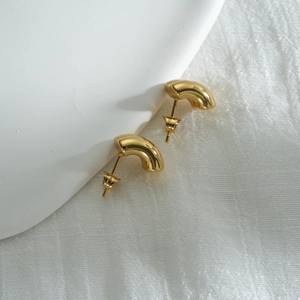 Detail of 18k gold geometric C-shape stud earrings on a minimalist white textured base