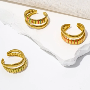 Detailed view of 18K gold plated striped enamel open rings on a white textured background