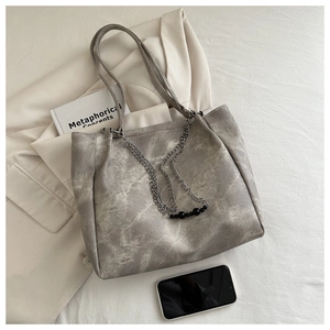Close-up of washed gray tote bag with metal chain on a white blazer background