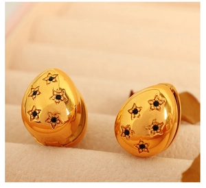 Detailansicht goldener Tropfenohrringe mit Sternenmustern und schwarzen Kristallen in Box