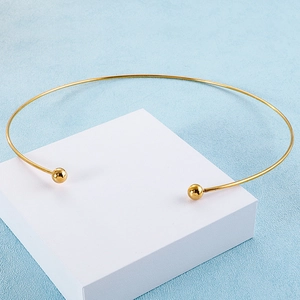 High angle shot of minimalist gold C-shaped titanium steel collar with ball ends on white cube