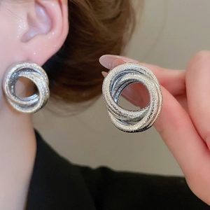 Macro shot of silver intertwined triple hoop stud earrings with a textured glitter finish