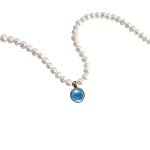 Detail of a white pearl necklace featuring a round blue birthstone pendant in a metal setting