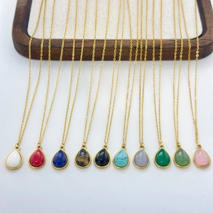 Collection of gold-plated necklaces with teardrop gemstone pendants on a wooden display stand