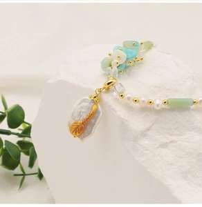 Close-up of baroque pearl pendant with golden leaf detail on white mineral stone
