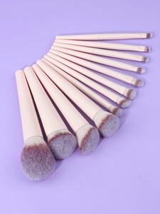 Flat lay of 13 professional pink makeup brushes with gradient bristles on purple background