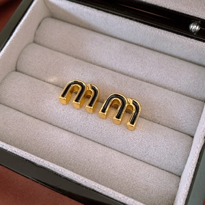 Detailed macro view of golden alphabet stud earrings with black enamel inlay in a box
