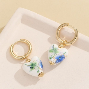 Golden heart earrings with blue floral ceramic charms on a beige textured tray
