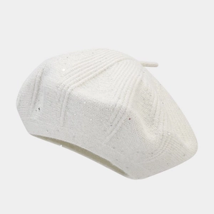 Close-up of white knitted beret featuring sparkling sequins and fine textured fabric
