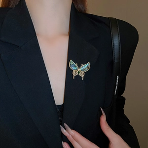 Détail d'une broche papillon avec ailes en nacre bleue et gemme verte sur un blazer