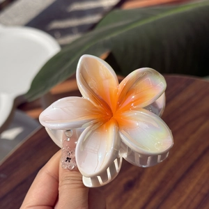 Close-up of plumeria hair claw clip with iridescent finish and orange gradient petals