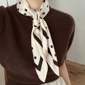 Close-up of beige silk scarf with black polka dots and border worn around the neck